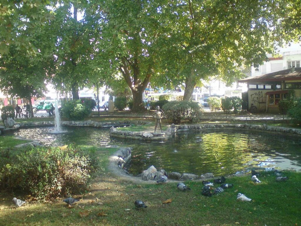 Ο Νικολάκης Τρίκαλα στην παλιά λιμνούλα της πλατείας, ανάμεσα σε πράσινο και δέντρα