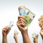 Χέρια υψώνουν χαρτονομίσματα ευρώ, συμβολίζοντας μεγάλα χρηματικά ποσά και επιδοτήσεις