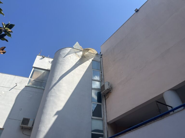 Αποκολλημένο τμήμα στέγης κρέμεται επικίνδυνα στο Πολιτιστικό Κέντρο Τρικάλων μετά το μπουρίνι, υπό το φως της ημέρας.