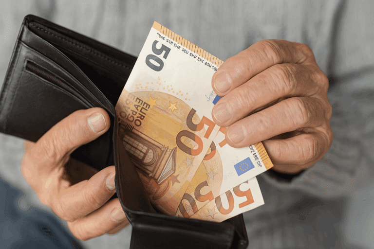 Χέρι ηλικιωμένου που βγάζει χαρτονομίσματα από πορτοφόλι, συμβολίζοντας το επίδομα των 250 ευρώ.