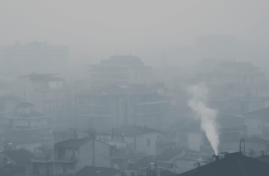Πόλη καλυμμένη από πυκνή ατμοσφαιρική ρύπανση με χαμηλή ορατότητα και καπνό από καμινάδα.